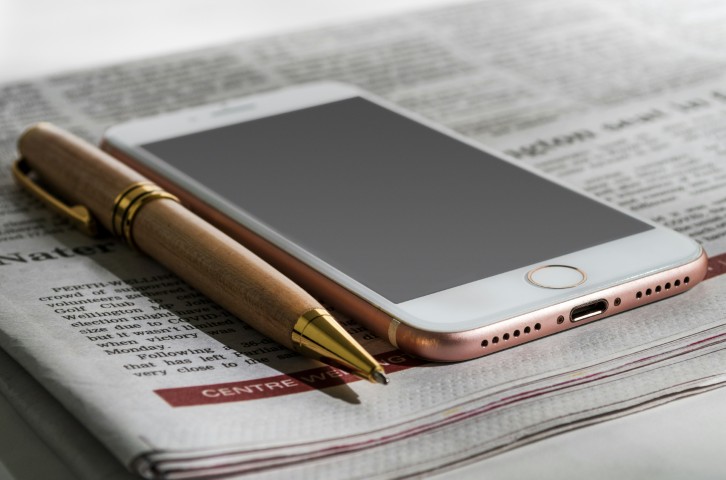 Phone and pen sitting upon a newspaper
